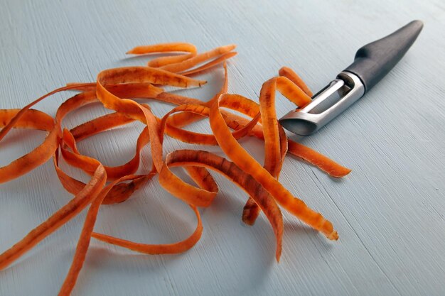 Snijdmes en wortelvel op een lichte houten tafel Schillen van groenten voor het koken