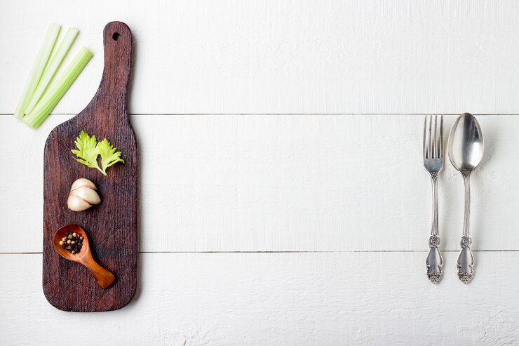 Snijplank, kruiden en bestek op wit houten