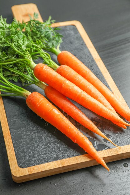 Snijplank met rijpe wortelen op zwarte tafel, bovenaanzicht