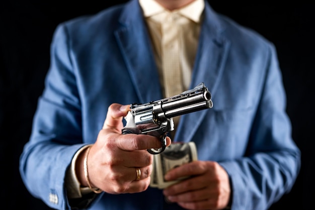 Sniper man in black suit gesturing and boldly holding gun on isolated black background