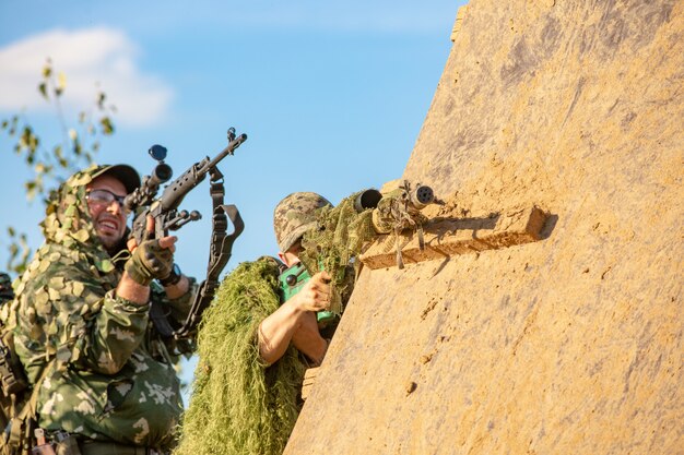 Sniper team armed with large caliber, sniper rifle, shooting enemy targets on range from shelter, sitting in ambush