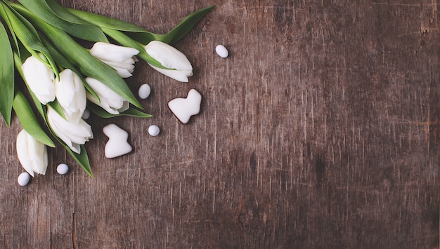 Snoepjes om Pasen te vieren. Witte tulpen, chocolade-eieren en konijn. Oude houten achtergrond.