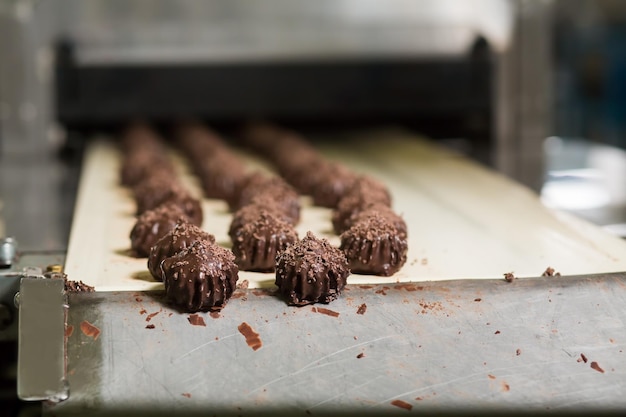 Snoepjes op de rand van de transportband. Donkerbruin snoep met schaafsel. Nieuw verbeterd recept van dessert. Minder suiker meer cacao.