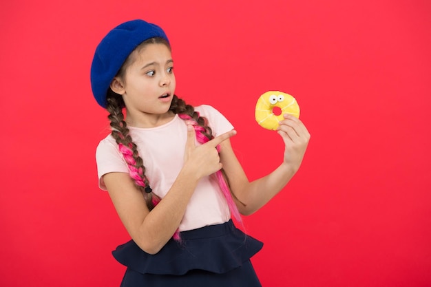 Snoepwinkel en bakkerijconcept Kinderen grote fans van gebakken donuts Onmogelijk om vers gemaakte donut te weerstaan Meisje houdt geglazuurde schattige donut in de hand rode achtergrond Kid speels meisje klaar om donut te eten