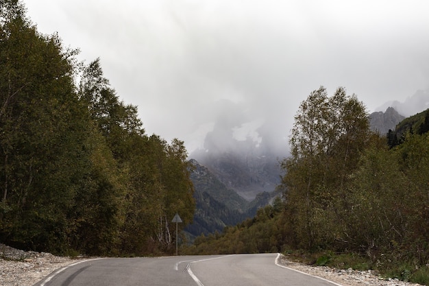 Catena montuosa ricoperta di neve tra le nuvole. strada. fitta foresta sui pendii della montagna caucaso, russia