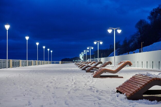 Snow covered bench by street light against sky during winter