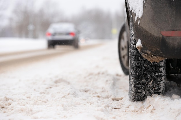 Snow covered car with studded wheels parked by the side of the road on a cold winter day