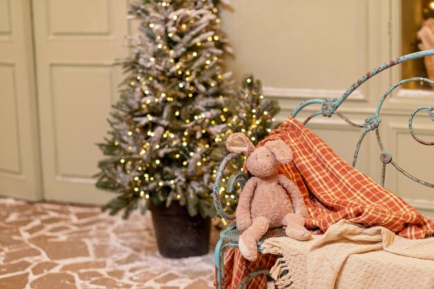 The snow-covered house is decorated for the new year. Vintage winter courtyard, decorated with Christmas trees, lanterns and a cozy bench with blankets and a plush hare. Soft selective focus.