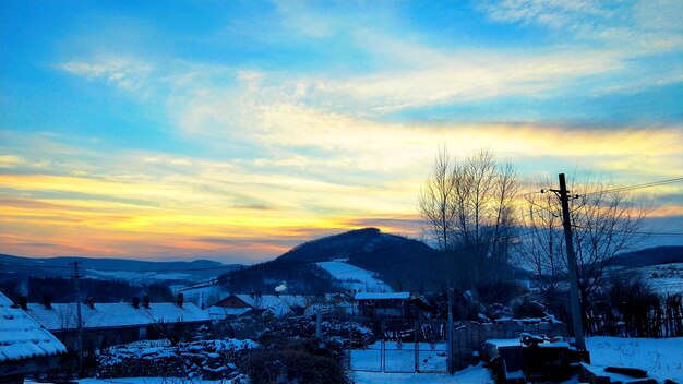 Snow covered houses against sky during sunset