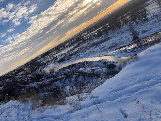 Snow covered land against sky during sunset