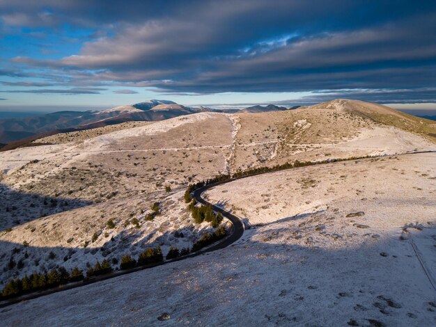 Snow covered mountains at sunset with a winding road in the foreground aerial view