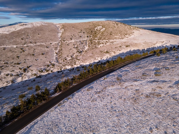 Snow covered mountains at sunset with a winding road in the foreground aerial view