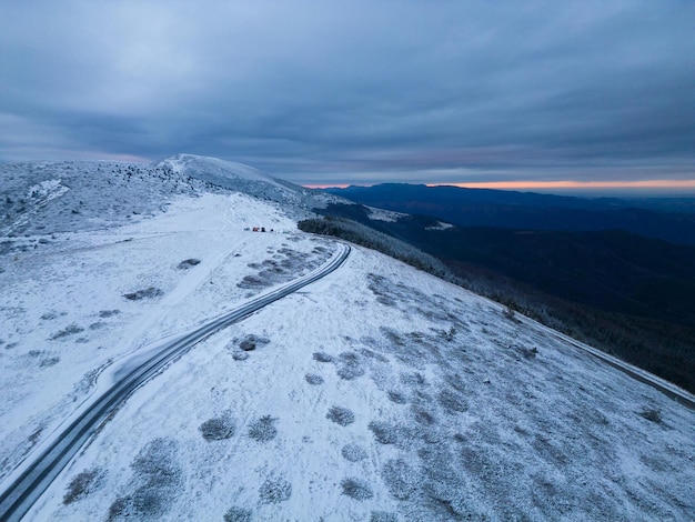 Snow covered mountains at sunset with a winding road in the foreground aerial view