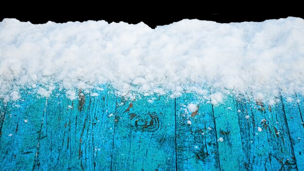 Photo snow-covered old blue boards on a black isolated background, winter background for design