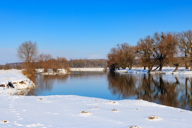 Riva del fiume coperta di neve al tramonto del giorno d'inverno