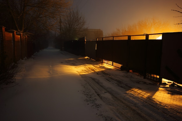 Snow covered suburban road lit by yellow lights at night time.