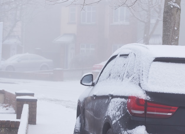 Snow on dark car body close up at snowy and fogy winter day.