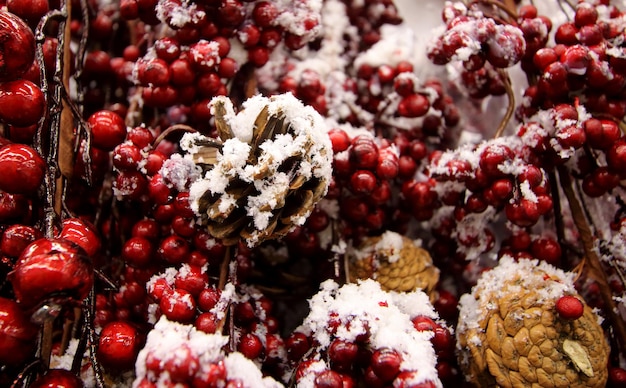 Snow on decorative red berries and pine cones