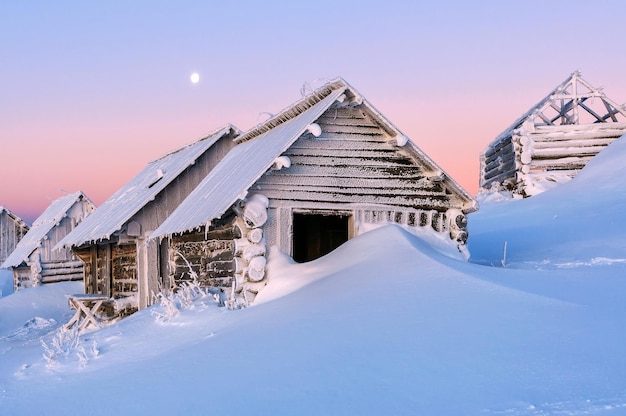 Snow drifts and abandoned log cabins in winter mountains