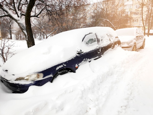 冬の激しいブリザード降雪吹雪の後、市の通りの私道の駐車場スポットカーのセダンのフロントガラスの窓に積もった雪の層雪の吹きだまりと極端な気象条件での車両