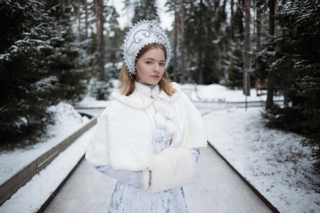 Photo snow maiden a cute young blonde in a white snow maiden costume with a kokoshnik in the forest among