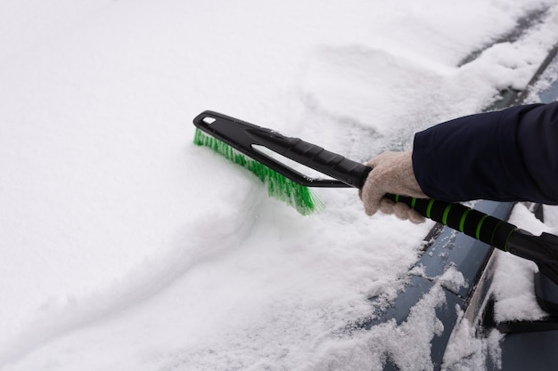 Snow removal, car in snow. Woman cleans the car from snow.