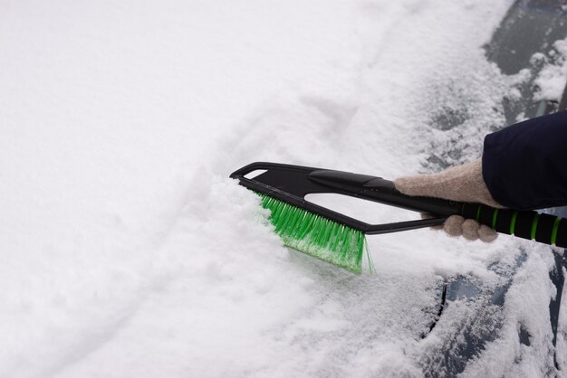 Snow removal, car in snow. Woman cleans the car from snow.