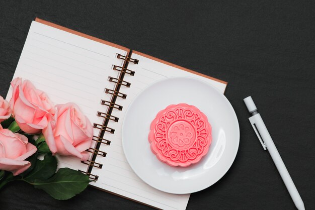 Snow skin mooncake and pink flowers. Open notebook with copy-space.