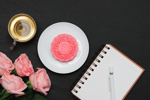 Snow skin mooncake and tea cup with flowers. Open notebook with copy-space.