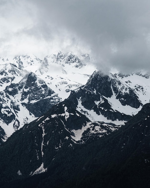 Snow on top of the mountain, beautiful photography of the foggy sky and winter mountains. Outdoor view, rocky cliff. Winter tourism.