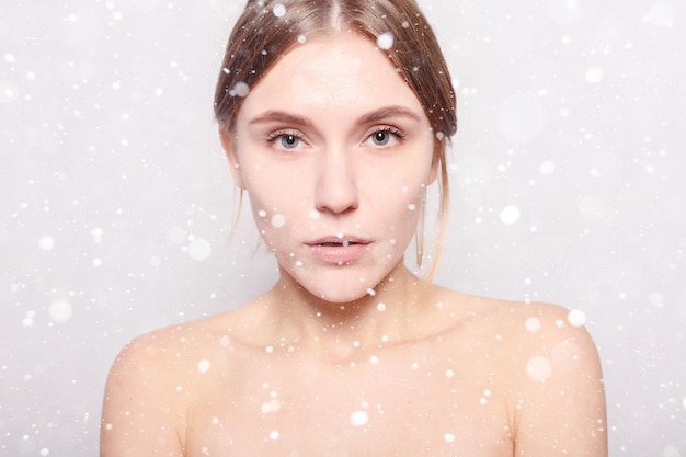 雪、冬、クリスマス、美容、スキンケア、そして人々のコンセプト-スパウーマン。入浴後の美少女が顔に触れた。彼女の柔らかい肌に触れている彼女の頭にタオルを持つ美女。雪の背景の上