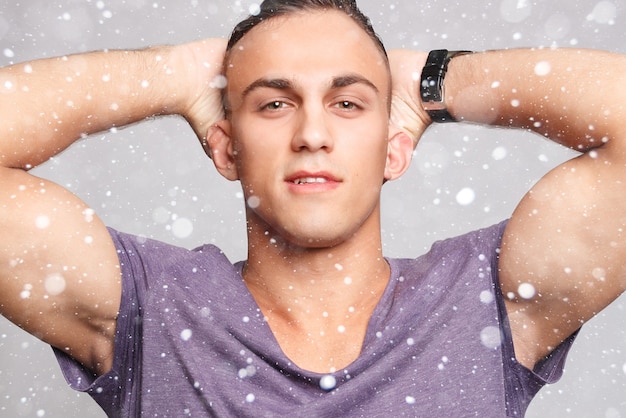 Photo snow, winter, christmas, emotion, advertisement and people concept - handsome young man over snow background looking at camera. portrait of laughing young man in pockets leaning against grey wall.