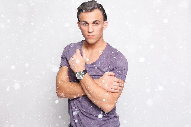 Snow, winter, christmas, emotion, advertisement and people concept - Handsome young man over snow background looking at camera. Portrait of laughing young man in pockets leaning against grey wall.