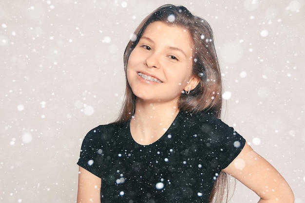 Snow, winter, christmas, health, people, dentist and lifestyle concept - Portrait of teen girl showing dental braces. candid portrait of a girl wearing braces, with hair motion over snow background