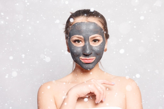 Snow, winter, christmas, people, beauty concept- woman face\
mask. portrait of beautiful girl removing cosmetic black peeling\
mask from facial skin over snow background