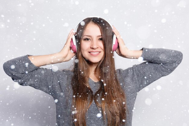 Snow, winter, christmas, People, leisure and technology concept - happy woman or teenage girl in headphones listening to music from smartphone and dancing over snow background