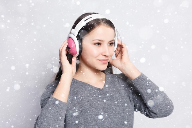 Snow, winter, christmas, People, leisure and technology concept - happy woman or teenage girl in headphones listening to music from smartphone and dancing over snow background