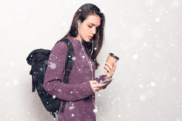 Snow, winter, christmas, technology, lifestyle, internet addiction and people concept - Young beautiful woman with smart phone. smiling attractive woman looking at the mobile phone snow background