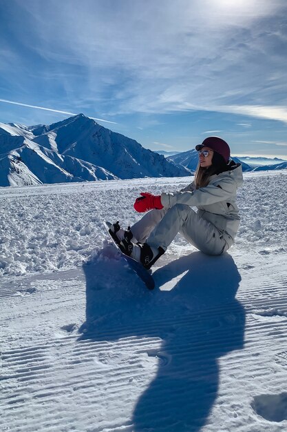 A snowboard rider girl sitting on a mountain slope relaxing and resting on a beautiful snow mountain slope.