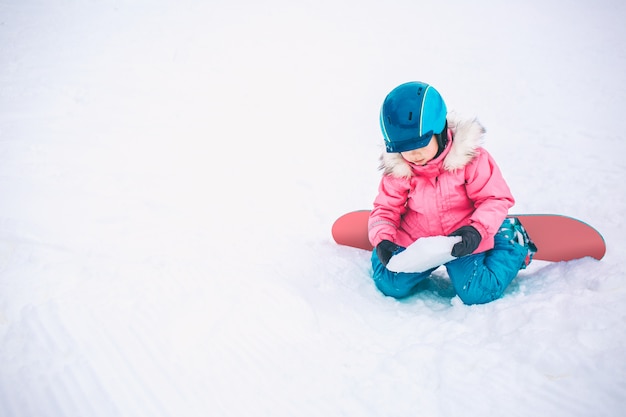 Snowboard Wintersport. Weinig jong geitjemeisje die met sneeuw spelen die warme de winterkleren dragen. Winter