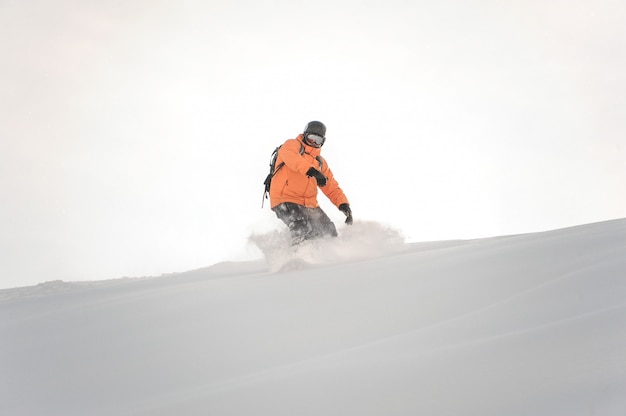 Snowboarder in oranje sportkleding rijden de berghelling tegen de witte hemel