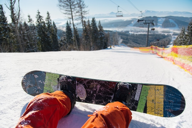 Snowboarder oogpunt op zijn voeten op de besneeuwde helling onder skilift op zonnige dag in de bergen