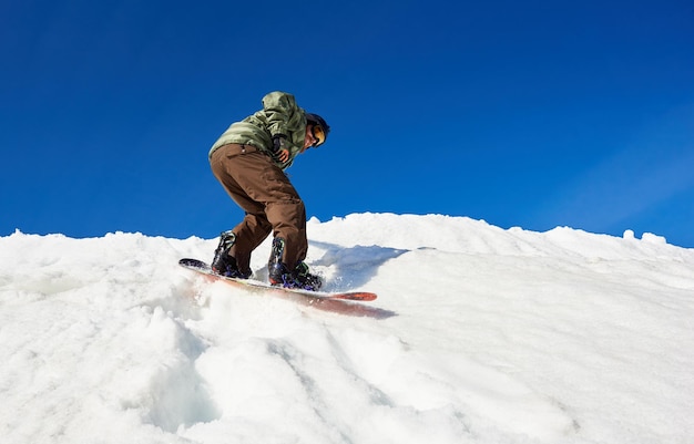 Snowboarder riding snowboard in deep snow down mountain slope on background of bright blue sky