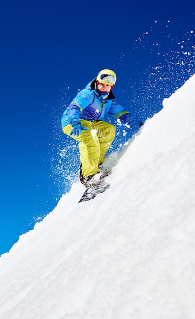 Snowboarder riding snowboard down snowy mountain slope on sunny winter day Extreme sport concept