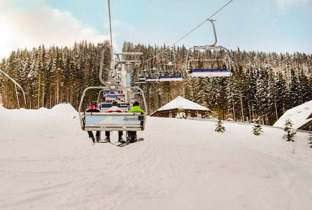 スノーボーダーとスキーヤーは、晴れた日の雪に覆われた森の雪に覆われた山へのスキーリフトに乗る