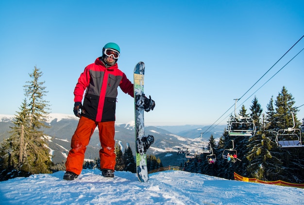 冬のスキーリゾートに乗った後、山の頂上に彼のスノーボードと立っているスノーボーダー
