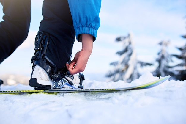 Сноубордист пристегивает ноги в ботинках для сноуборда в современных быстрых креплениях с ремнями Всадник на горнолыжном курорте готовится к сеансу фрирайда Мужчина в модной одежде