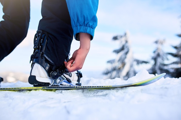 Snowboarder straps in his legs in snowboard boots in modern fast flow bindings with straps Rider at ski resort prepares for freeride session Man wearing fashionable outfit