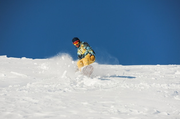 Snowboarder in stylish sportswear riding down the slope on sunny day in Georgia, Gudauri