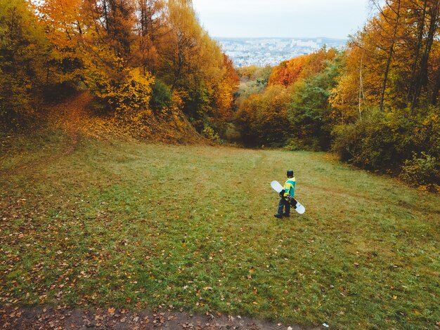 Snowboarder waiting for ski season standing on autumn slope